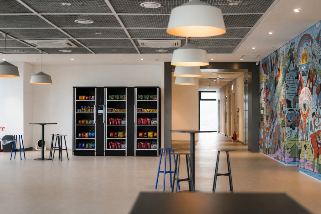 Trio smart fridge vending machine placed in a vibrant shared office and dining area.